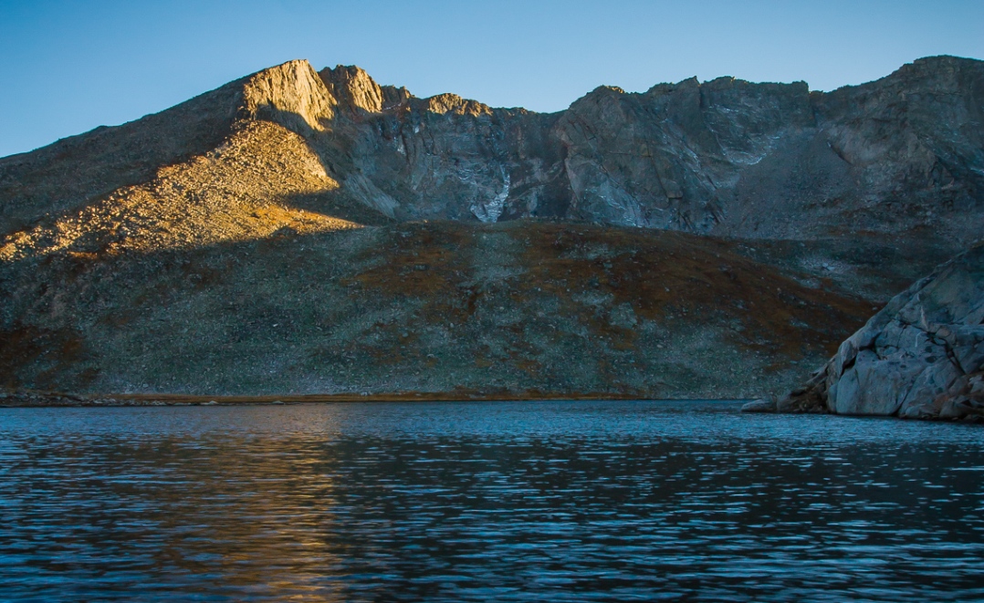 Mount Evans lit by the last few minutes of sunlight, reflected in the deep, dark blue waters of Summit Lake.